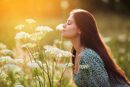 Young happy woman sniffing a tall white wildflowerの写真素材