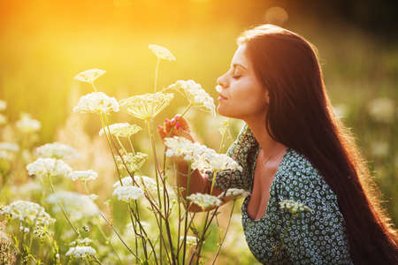Young happy woman in dress sniffs a tall white wild flowerの写真素材