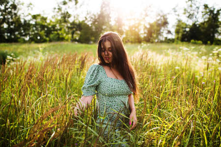 Happy young woman in green dress in the evening fieldの写真素材
