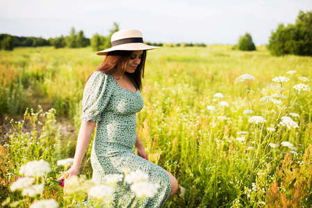 Beautiful young woman in a hat and with long hair walks in the fieldの写真素材