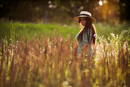 Happy young woman with long hair in a hat in a field in the eveningの写真素材