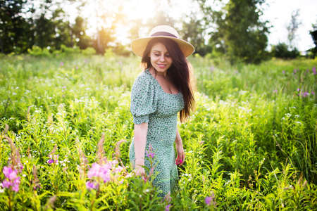Beautiful young woman in a hat walks in a field of wildflowersの写真素材
