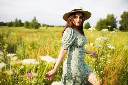 Happy young woman in a hat and with long hair walks in the fieldの写真素材