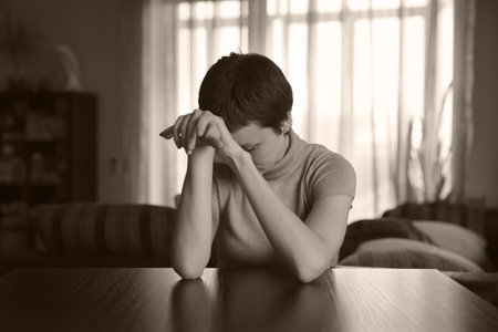 Pretty young woman sitting at a table and sadの写真素材