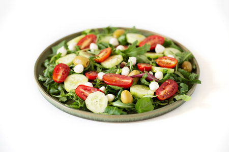 Salad made with arugula, tomatoes, cucumbers, mozzarella and olives in a green plate. Shot with a shallow depth of field.の写真素材