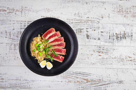 Fried pieces of tuna with kenoa and beans in a plate on a light background. Flat layの写真素材