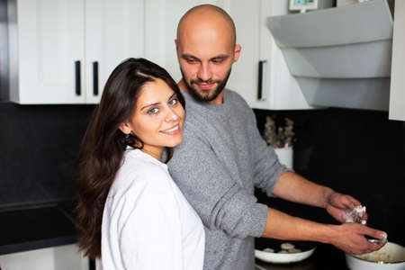 Young woman and man cooking together in the kitchen at homeの写真素材