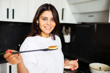 Girl prepares pancakes in the kitchen at home. She shows us a cooked pancakeの写真素材
