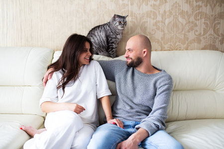 Young couple sitting on the sofa with their cat at homeの写真素材