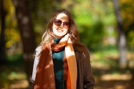 Beautiful young woman in sunglasses in the autumn forest. She smiles at the cameraの写真素材
