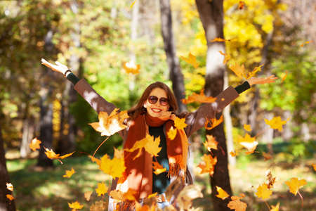 Joyful young woman throws maple leaves on a sunny autumn dayの写真素材