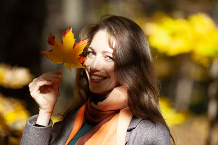 Young pretty woman holding maple leaves in her hand near her faceの写真素材