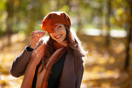 Young woman in beret holds a maple leaf near her faceの写真素材