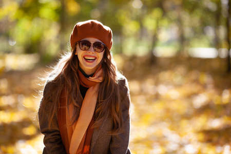 Joyful young woman in sunglasses and orange beret in autumn park on a sunny dayの写真素材