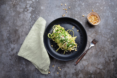 Spaghetti with spinach, pine nuts and parmesan in a plate on a gray table and a fork. Flat layの写真素材