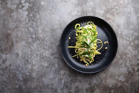 Spaghetti with spinach, pine nuts and parmesan cheese in a black plate on a gray table. Flat layの写真素材
