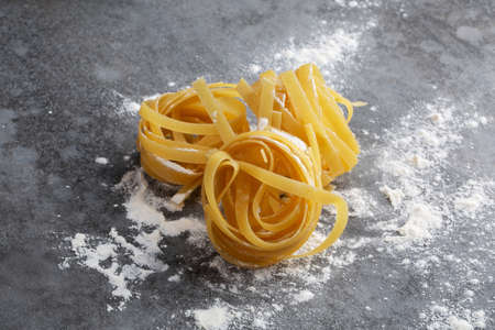 Rolled up spaghetti in flour lie on a gray tableの写真素材