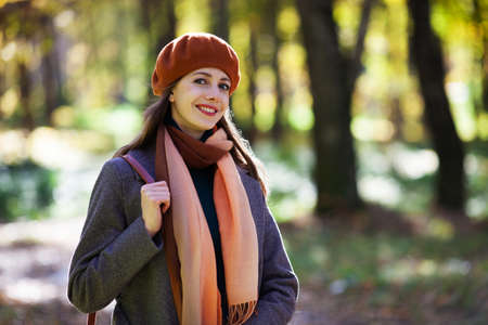 Young woman in an orange beret walks in an autumn park on a sunny dayの写真素材