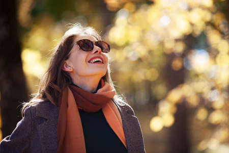 Portrait of young happy woman in sunglasses in sunny autumn forestの写真素材