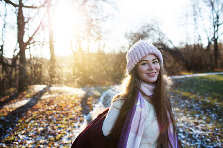 Happy beautiful girl in a knitted hat walks in the autumn park on a sunny dayの写真素材