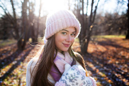 Beautiful girl in a knitted hat and mittens in a sunny autumn parkの写真素材