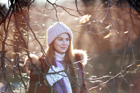 Beautiful girl in a knitted hat among the branches of a tree in a sunny autumn forestの写真素材