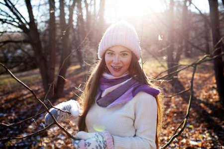 Beautiful young woman in a knitted hat and mittens in an autumn park on a sunny dayの写真素材