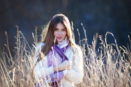 Beautiful long-haired girl stands in tall dry grass on a sunny autumn dayの写真素材