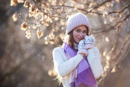 Beautiful girl in a knitted hat and mittens on a wood background with dry leavesの写真素材