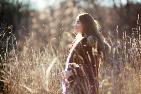 Beautiful young woman walking among tall dry grass in a fieldの写真素材
