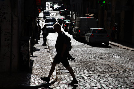 Silhouette of a man crossing a paved road on a sunny day in the street of a European cityの写真素材