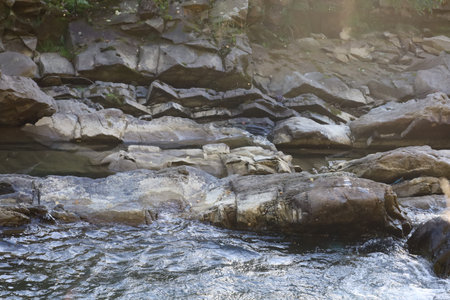 Rocky riverbank with sedimentary rock layers. Water below is turbulent, indicating fast flow and...