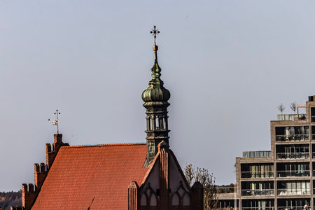 Contrast of an old red-roofed building with a green spire and a modern apartment complex under a...