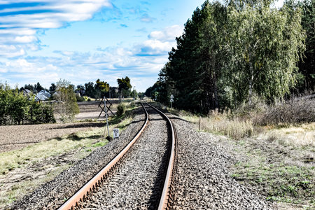 Railway track curving through rural landscape with fields, trees, and a small village on the left...