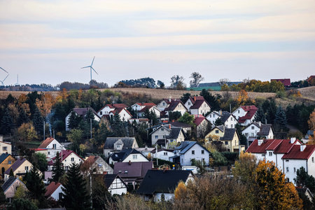 Small village on a hillside with diverse rooftops amid autumn trees and a bright white sky.