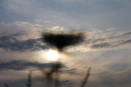 Sunlight pierces through elongated clouds, creating rays spreading across the sky, highlighting the...