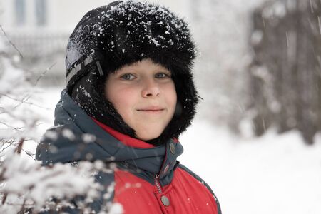 Smiling boy in a winter cap near  snow-covered bushの写真素材