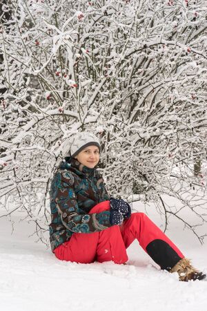 Beautiful girl in red pants sitting in the snow under the snowyの写真素材