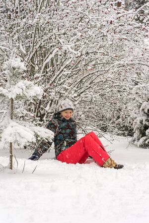 Girl sitting in the snow under the -covered bush rosehipの写真素材