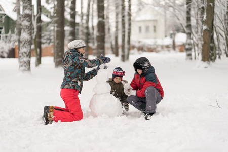 Mother and two sons play  molded from snow snowmen in the winの写真素材