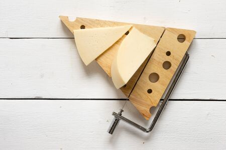 Cheese on a cheese cutter against a white wooden tableの写真素材