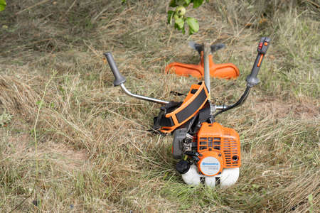 Minsk, Belarus - 02/08/2020 Petrol scythe trimmer brushcutter Husqvarna 143R-II lies on the mown hay after mowing tall grass in the garden of a country house.のeditorial素材