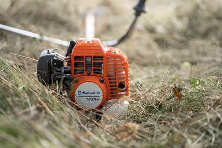 Minsk, Belarus - 02/08/2020 Petrol scythe trimmer brushcutter Husqvarna 143R-II lies on the mown hay after mowing tall grass in the garden of a country house.のeditorial素材