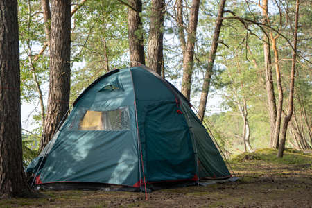 A large tourist tent is set up on the campground in a beautiful forest by the lake. Camping with a tent. Self-isolation in the forest during the COVID-19 quarantine.の写真素材