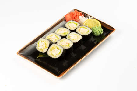 A portion of maki sushi with an assortment of Japanese side dishes in a rectangular ceramic plate on a white plate.の写真素材