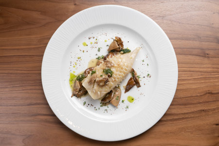 Beautifully cooked fried squid carcass with wild mushrooms and herbs in a white plate on a wooden...