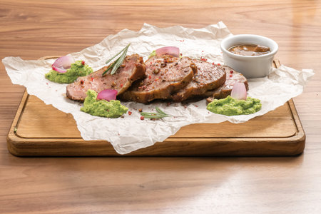 Pieces of roast pork with spices, rosemary, pea puree and sauce on a wooden table