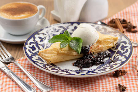 Puff pastry dessert with berry jam and a ball of vanilla ice cream decorated with a mint leaf in a plate with a traditional Uzbek patternの写真素材