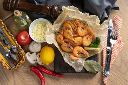 Boiled king prawns with lemon in baking paper on a wooden chopping boardの写真素材