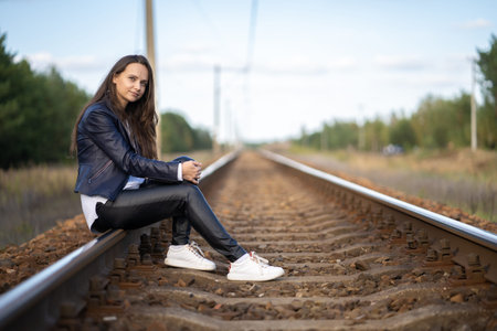 A young beautiful single woman is sitting on the railway tracks waiting for a train locomotive on a clear summer dayの写真素材
